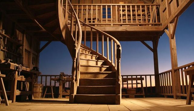 Curling wooden spiral staircase in rustic timber workshop loft at dusk, warm golden light