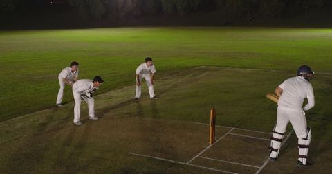 Night cricket batsman facing close-in fielders on illuminated wicket under floodlights