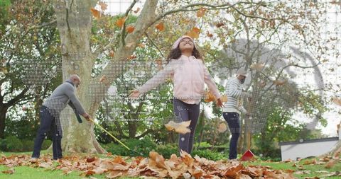 Multigenerational family raking leaves while child tossing autumn foliage in backyard