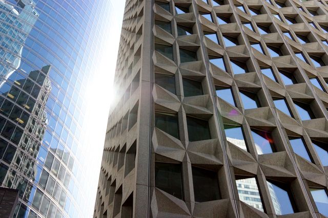 Close-up of two contrasting buildings featuring modern glass and textured façades in a city. Sunlight peeking through the gap, highlighting the architectural styles. Ideal for use in articles or presentations about urban design, architectural trends, or city development. Suitable for illustrating the juxtaposition of traditional and modern architectural elements in educational materials.