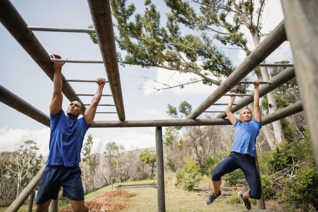 Fit man and woman climbing monkey bars during obstacle course in boot camp