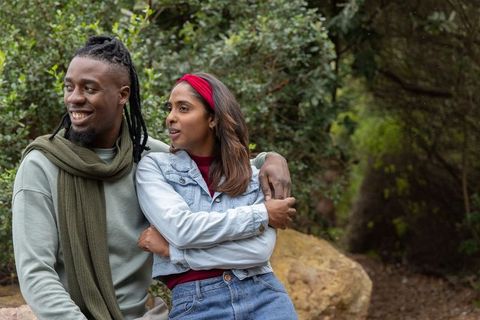Smiling diverse couple embracing on park boulder, enjoying outdoor nature moment