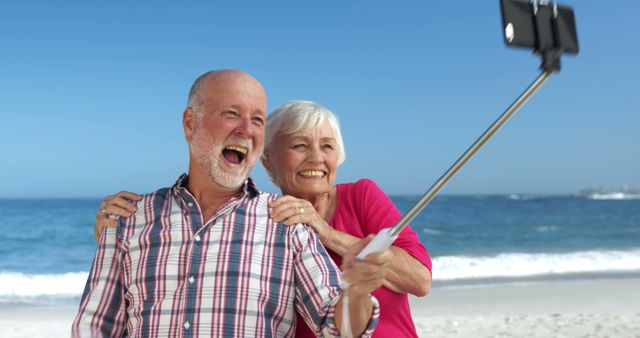 Happy senior couple taking selfie by beach shows enjoyment of retirement and leisure time. This image is ideal for advertisements or content promoting retirement, travel, healthy living for seniors, or family bonding stories. Can also be used for greeting cards or social media posts celebrating moments and memories.