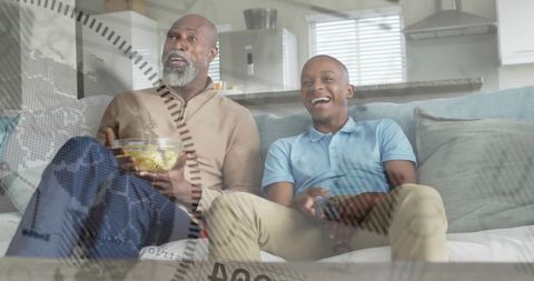 Father and Teen Watching TV on Couch Holding Remote and Snacks in Modern Open-Plan Home