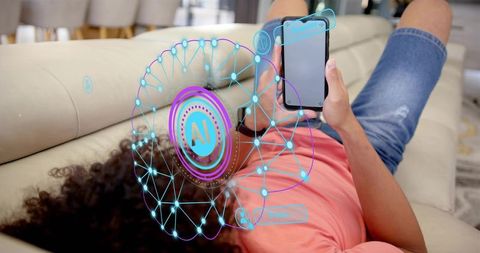 Young man lounging on sofa holding smartphone displaying ai holographic interface and wearable smart