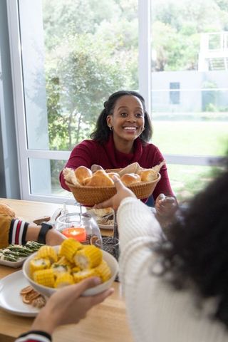 Friends passing dishes at cozy daylight dining table reaching for bread basket