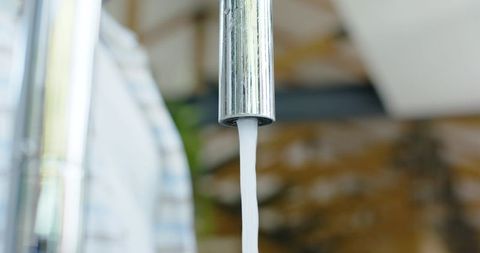 Chrome faucet pouring steady water stream into bathroom sink with towel and reflections