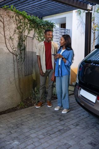 Stylish couple with car key fob by black suv under pergola