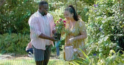 Couple exchanging potted flowers in sunny garden sharing plant care and outdoor leisure
