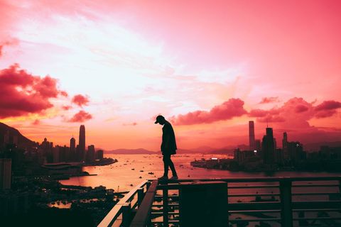 Silhouette of Person Walking on Rooftop at Sunset with City Skyline