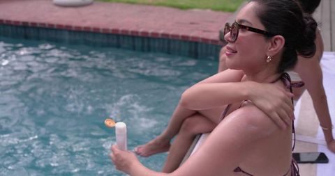 Diverse women relaxing by backyard pool holding sunscreen and wearing sunglasses