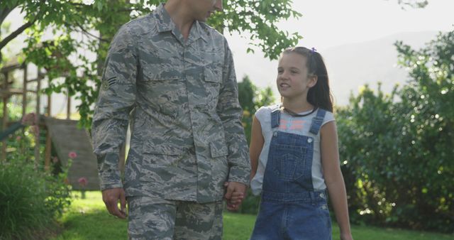 Caucasian male soldier holding hands with smiling daughter in garden, copy space. Soldier, armed forces, home coming, patriotism and defence concept, unaltered.