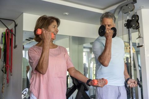 Senior couple exercising with dumbbells in home gym smiling and encouraging each other