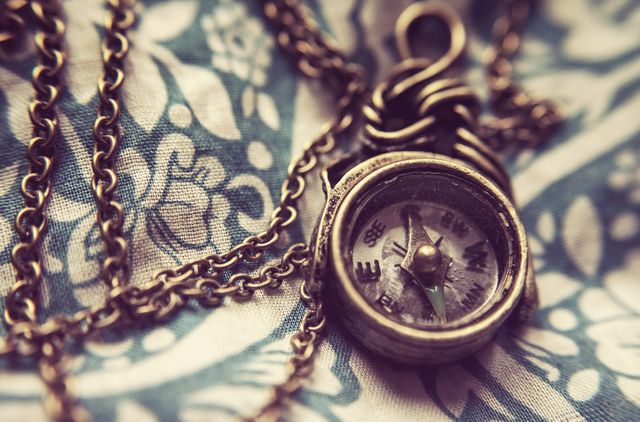 This charming visual captures a vintage compass pendant lying on floral fabric, perfect for new design concepts, adventure and travel items, or bohemian and rustic themed projects. Its intricate detail and classic appearance highlight timeless style and direction.
