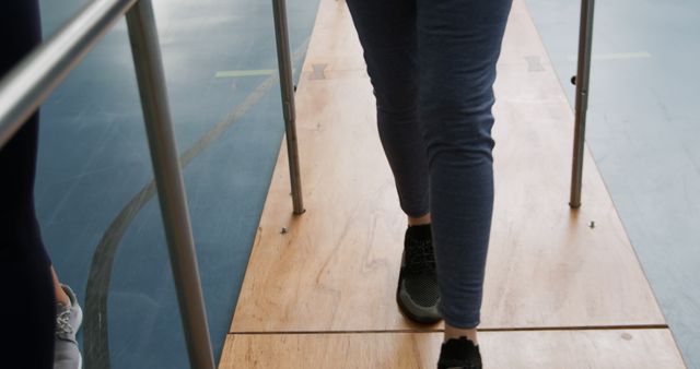 Person in a gym undergoing rehabilitation using parallel bars, suggesting efforts to regain mobility and strength. Useful for physical therapy concepts, medical training materials, and health recovery promotions.