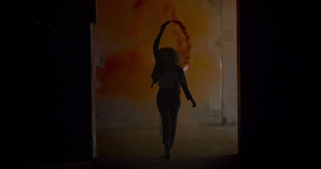 Young Caucasian woman performs a fiery dance in a dark setting. Her silhouette stands out against the dramatic backdrop of flames and smoke.