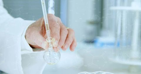 Senior scientist holding pipette transferring liquid into round-bottom flask in clean lab