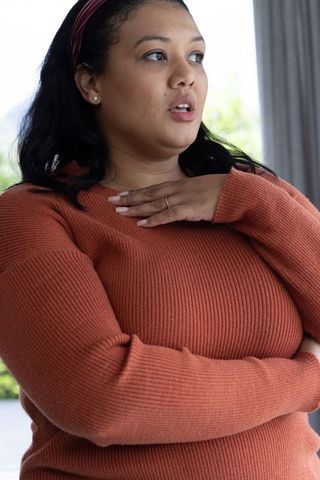 Surprised african american woman holding hand to chest wearing rust sweater, maroon headband