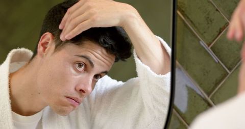 Caring man examining hair and face reflecting self-care routine
