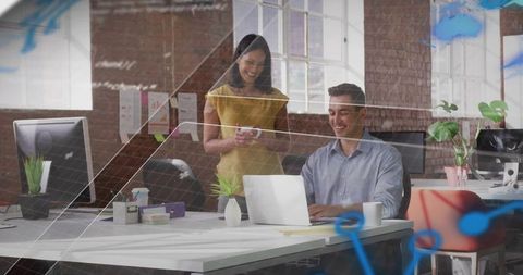 Smiling coworkers collaborating at laptop in modern open-plan office with natural light
