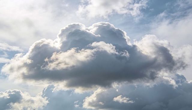 Billowing cumulus cloud catching sunlight with silver edges over vast blue sky