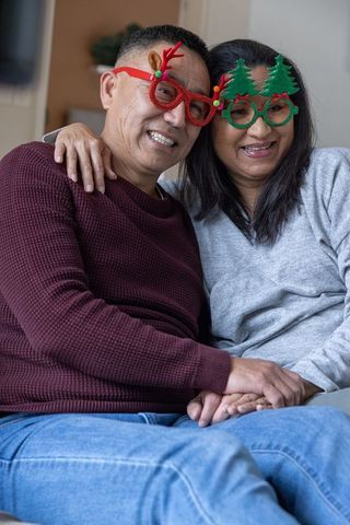 Happy Couple Wearing Festive Christmas Glasses Relaxing at Home