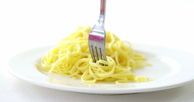 A fork twirls a portion of cooked spaghetti on a white plate, with copy space. Capturing the simplicity of a classic pasta dish, the image evokes the pleasures of Italian cuisine.