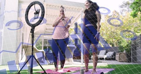 Two women filming backyard yoga with ring light and smartphone fitness influencers at home