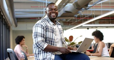 Entrepreneur Smiling Confidently with Laptop in Modern Office