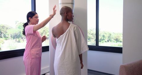 Technician positioning african american patient for mammogram in bright clinic room