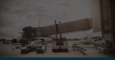Narrow-body airliner docked at jet bridge with vehicles servicing airport apron and ramp