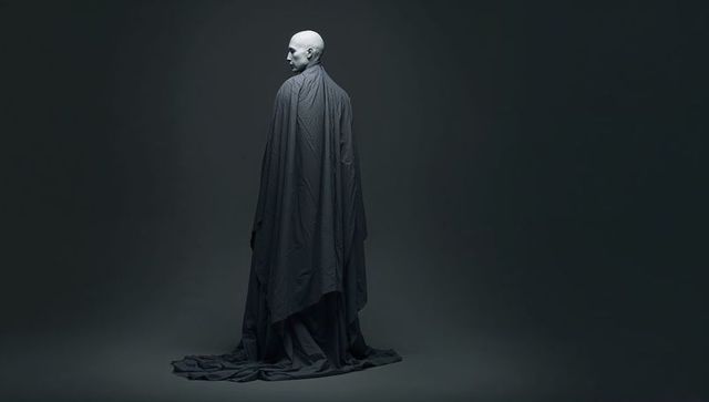 Solitary Bald Figure Standing in Draped Cloak Turning Head Left in Minimalist Monochrome
