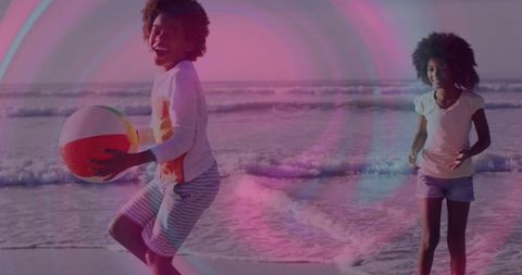 Happy children playing with beach ball by ocean at sunset