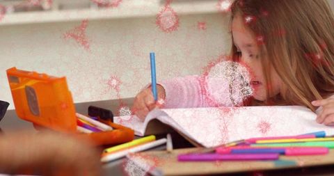 Young girl writing in notebook at desk with colorful markers and orange pencil case