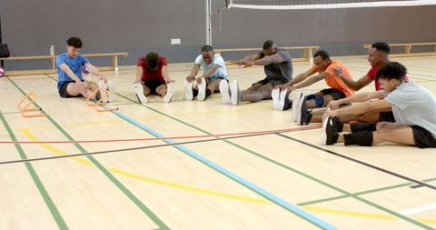 Male volleyball players stretching on indoor court during warmup and agility drills