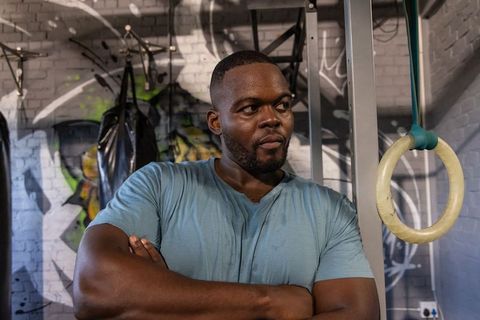 Muscular african american man standing focused in graffiti gym with arms crossed near rings