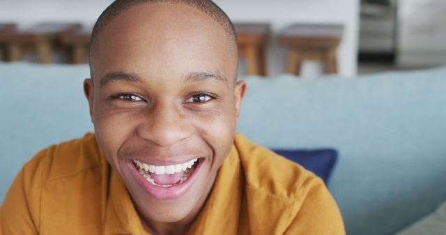Young man with a bright smile looking directly at the camera, conveying joy and positivity. Perfect for use in advertisements, promotional materials, or social media posts that aim to evoke happiness and a friendly atmosphere. The background suggests an indoor, modern setting, great for lifestyle and personal branding content.