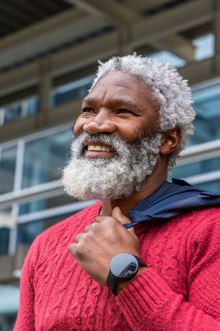 Confident mature man holding jacket over shoulder smiling in red sweater and smartwatch