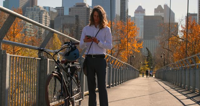 Man standing on urban bridge with bicycle using smartphone on sunny autumn day - Download Free Stock Images Pikwizard.com