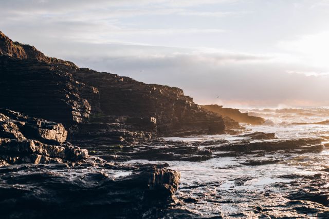 Rocky coastline captures the beauty of nature at sunset with waves crashing against the rocks. Ideal for travel blogs, nature publications, or relaxation backgrounds, highlighting natural landscapes and serene ocean views.