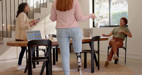 Coworker walking with prosthetic leg joining sunlit modern office meeting, collaborating