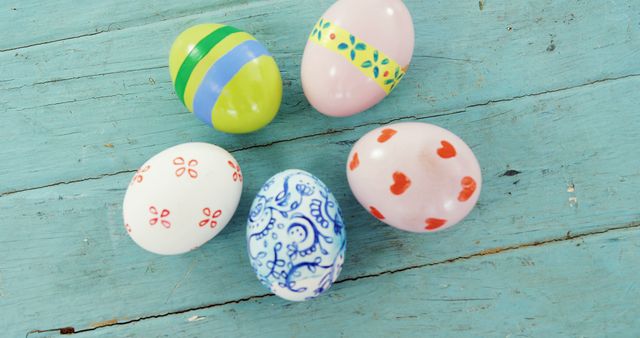 Colorful painted eggs are scattered on a rustic blue wooden surface, symbolizing Easter celebrations. Their vibrant patterns and designs evoke the festive spirit of the holiday.