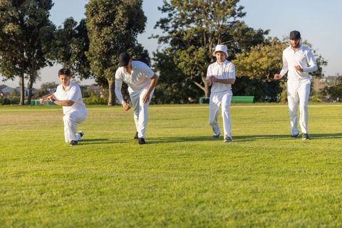 Cricket teammates walking across sunlit grass oval at golden hour in white uniforms