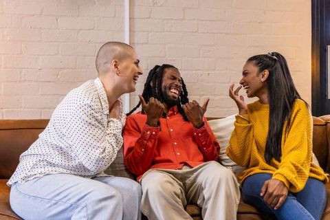 Diverse friends laughing together on cozy leather sofa sharing warm conversation and joy