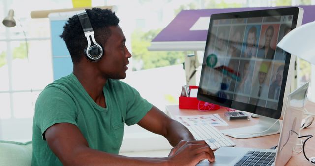 Man wearing headphones using desktop computer for video conferencing in bright, modern home office. Ideal for remote work, technology, and telecommunication concepts. Useful for promoting work-from-home solutions, digital nomad lifestyle, and modern office setups.