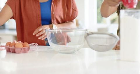 Diverse friends pouring flour through sieve into glass bowl preparing baking together