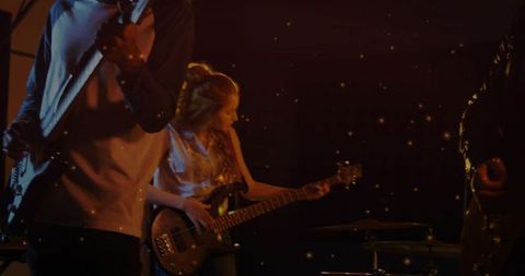 Female bassist playing electric bass on intimate stage with amber moody lighting and band