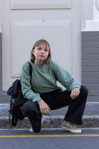 Young woman squatting on curb in casual streetwear with backpack and pale green sneakers