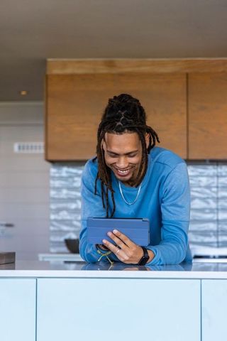 African american man leaning on kitchen island smiling and using tablet in modern home