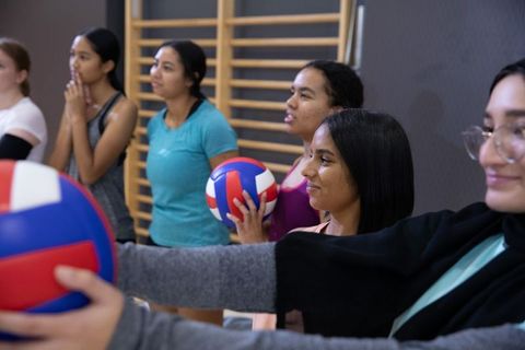 Diverse teenage girls practicing volleyball in school gym holding red white blue balls